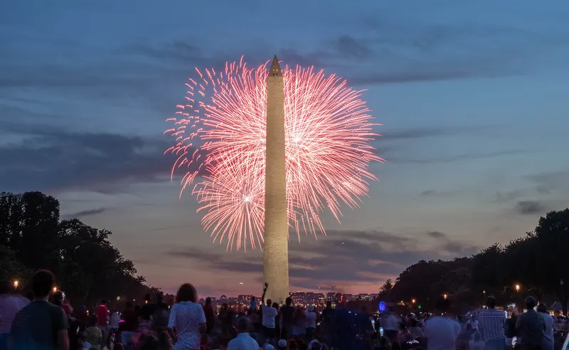 Fireworks bursting beside the floodlit Washington Monument over a crowd on the National Mall on the Fourth of July in Washington, D.C.